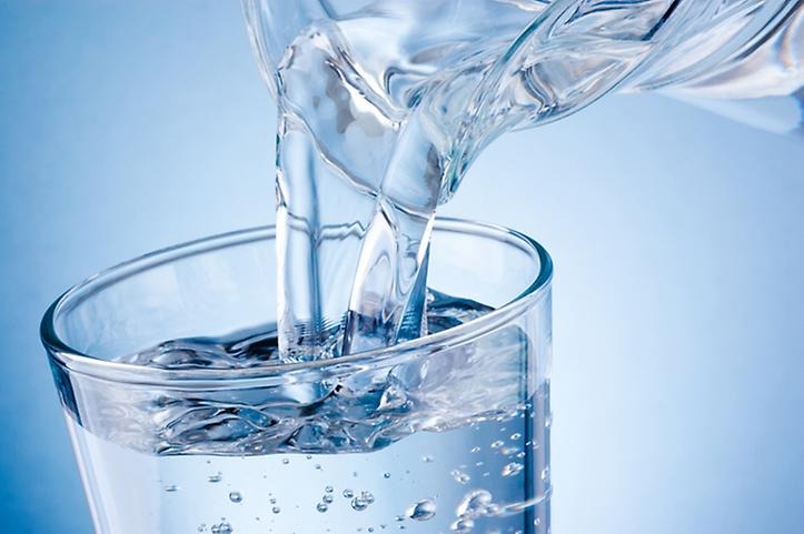 Häller vatten från en bringare till ett glas mot en blå bakgrund.
